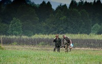 A bit of heavier weather is moving in, and a pair of hunters walk their gear out of the field. The doves won't move much in steady rain. At the left of image is one of the huntmaster's station stakes: the field is dotted with them to indicate approved shooting positions.