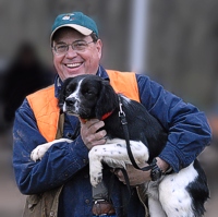 One of the perks of being Brittany-sized is the inevitable hoist up to the better viewing angle. This handler's smiling for the photographer, but his dog cannot tear his eyes away from the Junior bird field, where a brace is working.