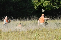 In a senior test, judges may tell the backing dog's handler to crouch with the dog and keep it steady while the other handler flushes up a bird. Here, that other handler's reminding his dog to stay put as that bird rises.